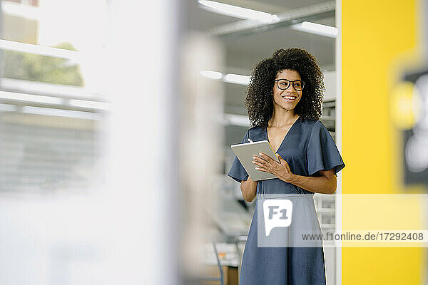 Smiling businesswoman looking away while holding digital tablet at office