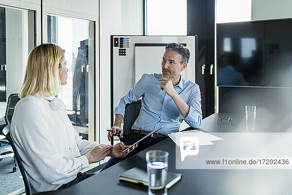 Mature businessman looking at female entrepreneur discussing while sitting in office