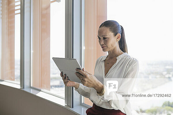Ältere Unternehmerin benutzt digitales Tablet am Fenster im Büro