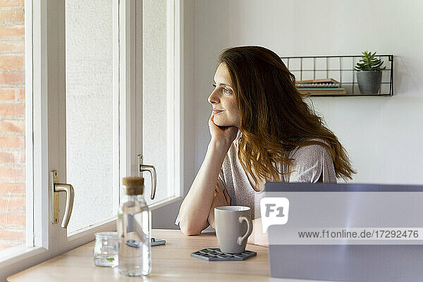 Thoughtful woman looking through window at home office