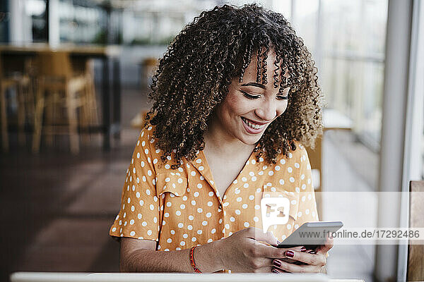 Lächelnde junge Frau  die in einem Café eine SMS schreibt