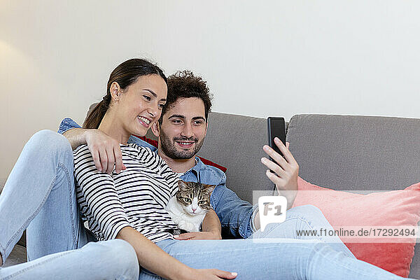 Smiling couple with cat taking selfie through smart phone at home