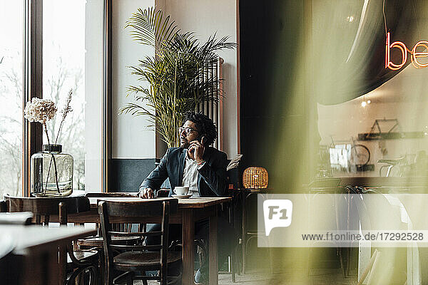 Männlicher Berufstätiger  der in einem Café sitzend mit seinem Smartphone telefoniert