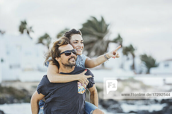 Smiling woman pointing while piggybacking on man at beach