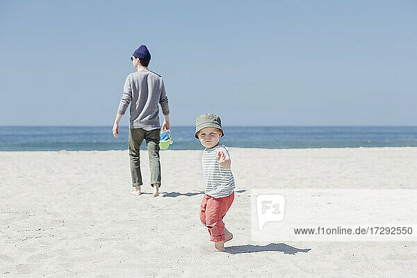 Kleiner Junge spielt  während sein Vater am Strand spazieren geht