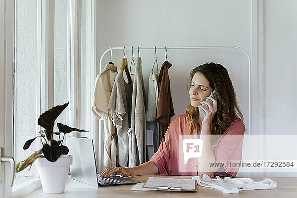 Geschäftsfrau  die einen Laptop benutzt  während sie zu Hause mit dem Handy telefoniert