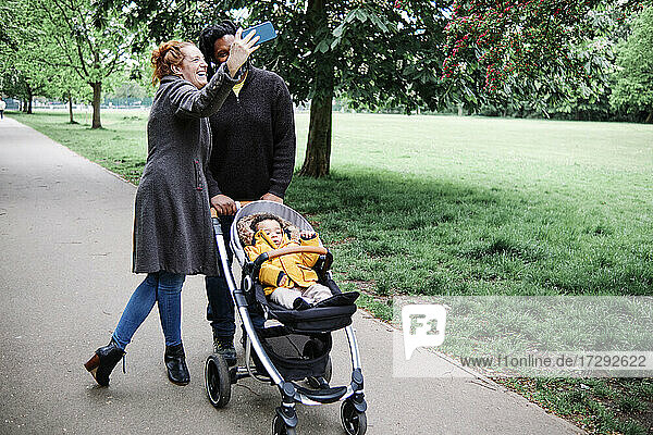 Glückliche Eltern mit Kinderwagen nehmen Selfie im Park