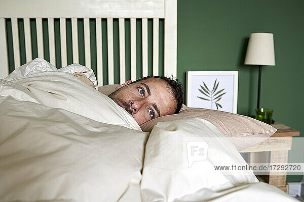 Man contemplating while lying in bed at home