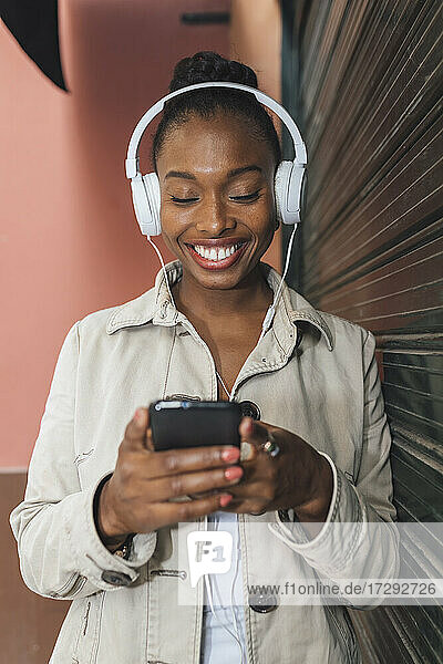 Happy woman wearing headphones text messaging through mobile phone while listening music by shutter
