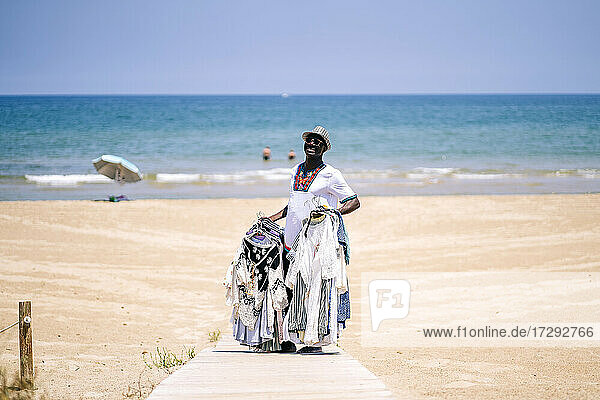 Male vendor standing on boardwalk while selling clothes at beach during sunny day