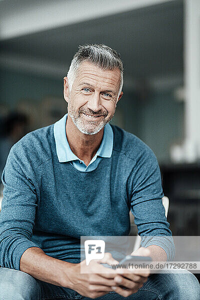 Smiling businessman holding mobile phone while sitting at cafe