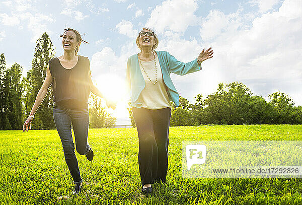 Glückliche Frauen  die sich beim Laufen auf einer Wiese an den Händen halten