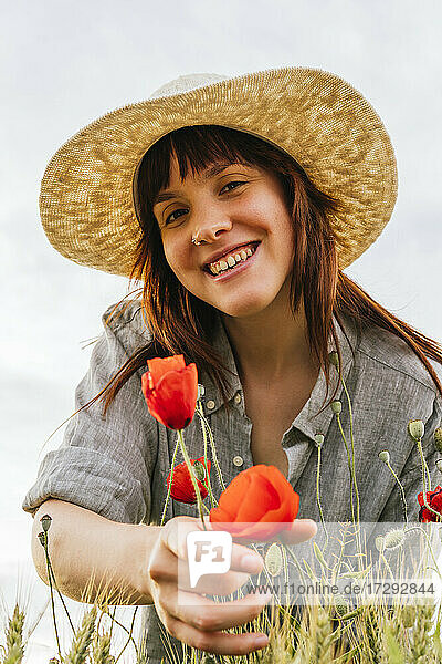 Smiling beautiful woman wearing hat plucking poppy flowers