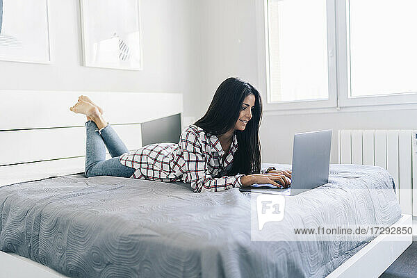 Junge Frau  die auf dem Bett liegend einen Laptop benutzt