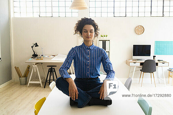Geschäftsfrau übt Yoga im Schneidersitz auf dem Schreibtisch im Büro
