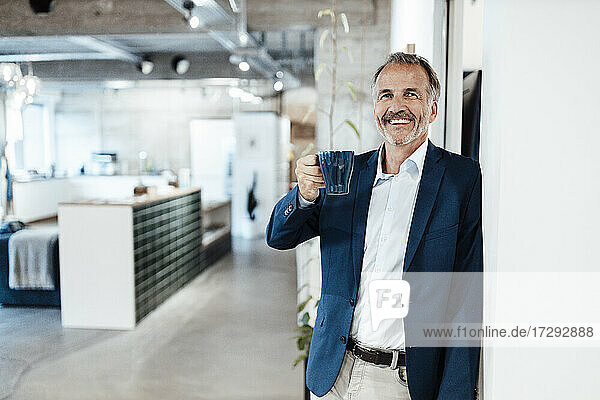 Männlicher Unternehmer mit Kaffeetasse  der sich an die Wand lehnt