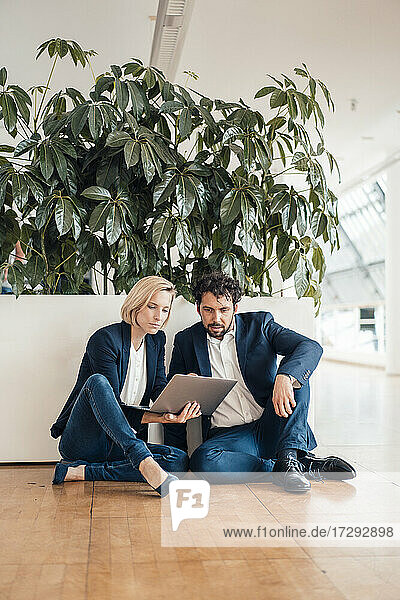 Business partners using digital tablet while sitting on floor in office