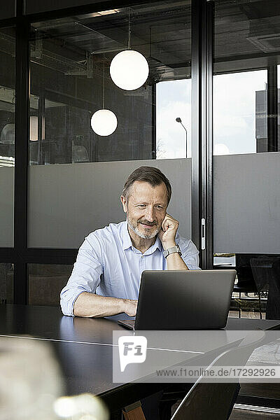 Lächelnder Geschäftsmann arbeitet am Laptop am Schreibtisch im Büro