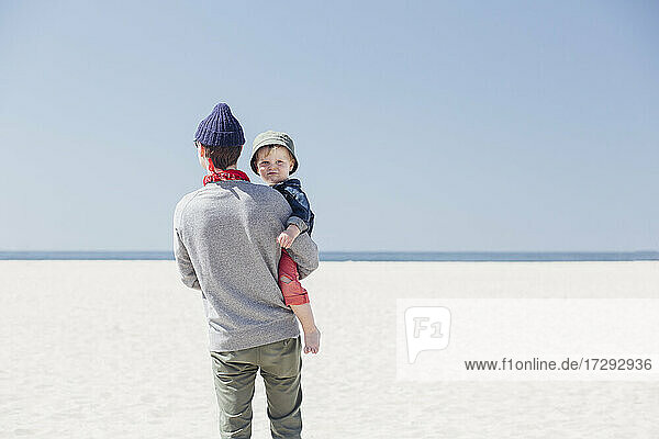 Man carrying son while standing at beach during sunny day