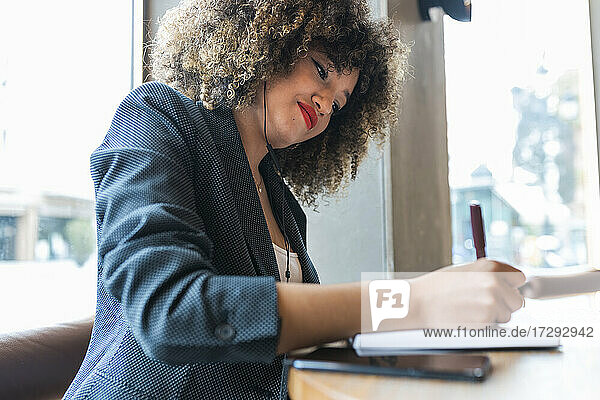 Afro-Geschäftsfrau schreibt in einem Café in ihr Tagebuch