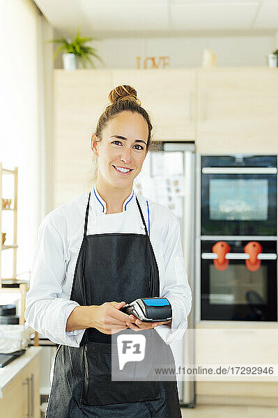 Lächelnde Köchin mit Kreditkartenleser im Restaurant