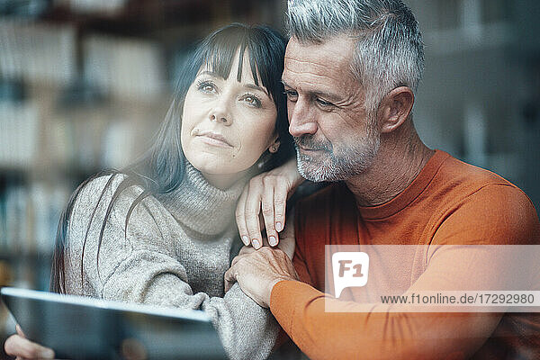 Woman day dreaming while leaning on man using digital tablet at coffee shop