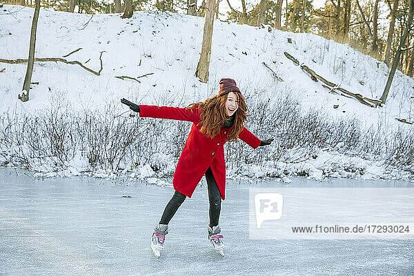 Cheerful woman with arms outstretched enjoying ice-skating on frozen lake