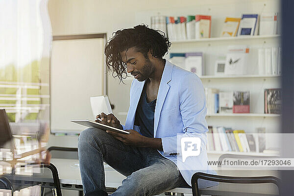 Junger Geschäftsmann  der ein digitales Tablet benutzt  während er auf dem Schreibtisch im Büro sitzt