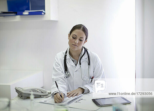 Weiblicher Arzt schreibt Bericht  während er am Tisch sitzt