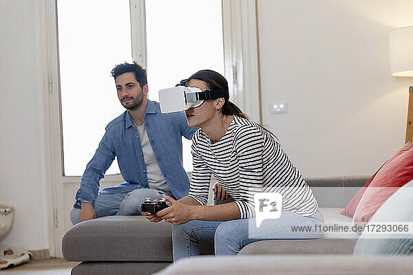 Young woman playing with virtual reality simulator by boyfriend at home