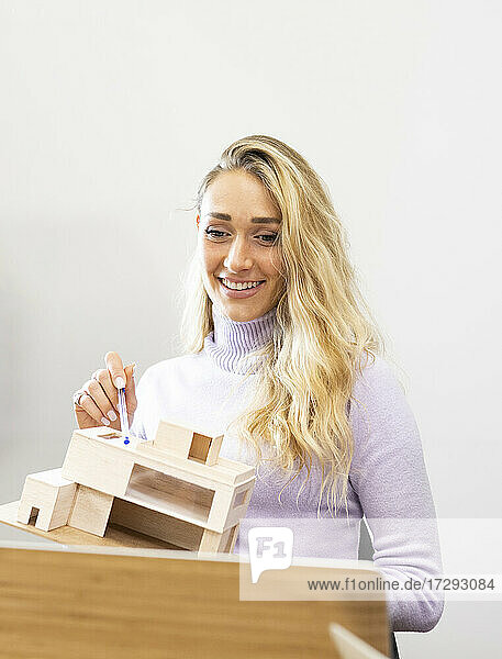 Lächelnde blonde Geschäftsfrau  die ein Modellhaus per Videoanruf im Büro erklärt