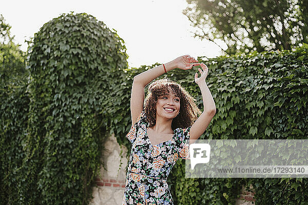 Glückliche junge Frau mit erhobenen Armen beim Tanzen im Garten