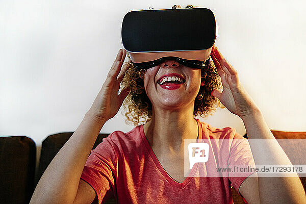 Fröhliche junge Frau mit Virtual-Reality-Simulator im Wohnzimmer