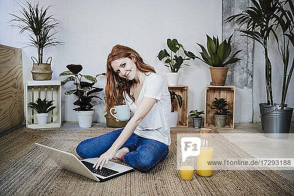 Junge Frau  die einen Laptop benutzt  während sie zu Hause auf dem Boden Kaffee trinkt