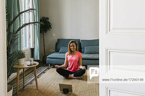Junge Frau meditiert im Wohnzimmer zu Hause