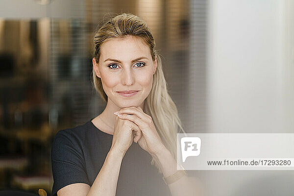 Beautiful smiling female entrepreneur sitting with hand on chin in office
