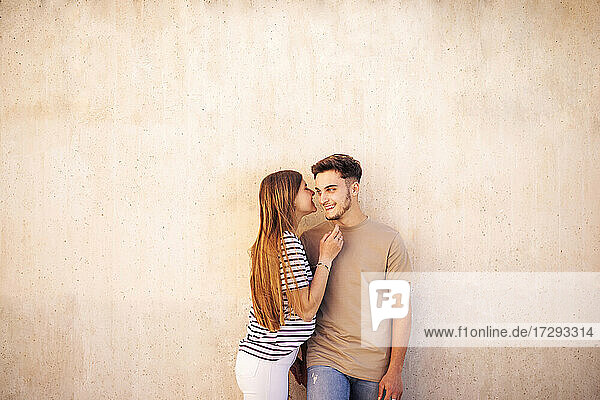 Lächelndes Paar steht zusammen vor einer beigen Wand