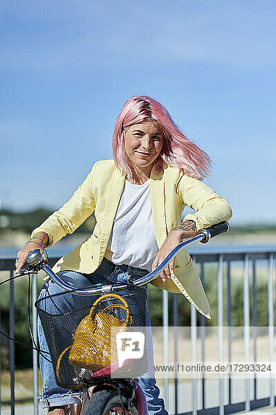 Lächelnde Frau mit Fahrrad am Geländer an einem sonnigen Tag