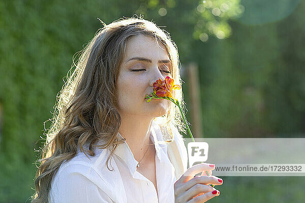 Junge Frau mit geschlossenen Augen riecht an einer Freesienblüte an einem sonnigen Tag