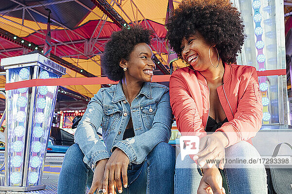 Happy female friends talking with each other while sitting in amusement park