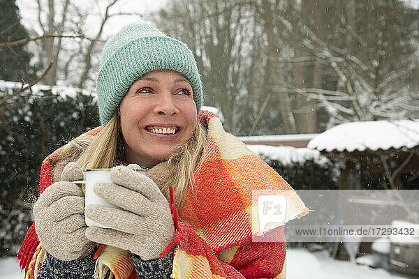 Fröhliche Frau mit Kaffeetasse  die bei Schnee wegschaut