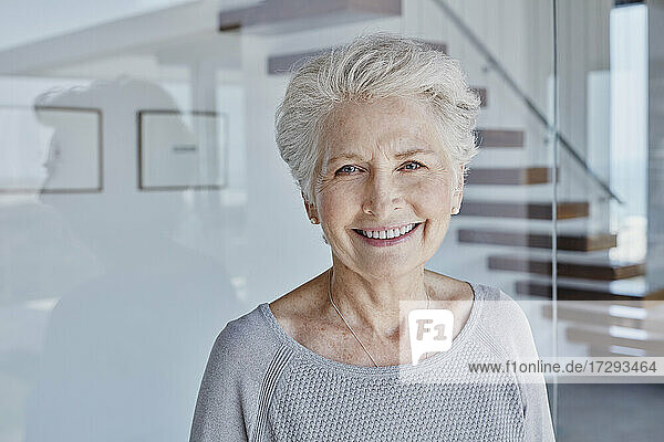 Happy senior woman standing in front of glass wall