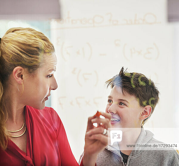 Mutter sieht ihren lächelnden Sohn an  während sie Mathematik an einem Glas unterrichtet