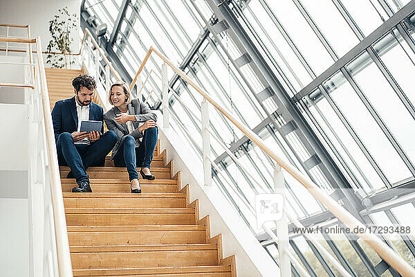 Geschäftsmann benutzt ein digitales Tablet  während er neben einem Kollegen auf einer Treppe sitzt