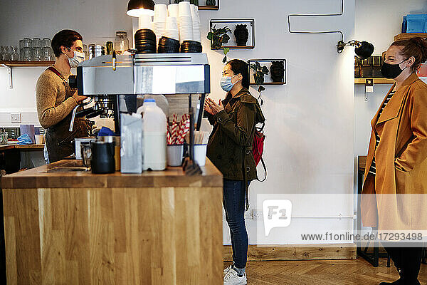 Frau gestikuliert während eines Gesprächs mit dem Besitzer am Tresen eines Cafés während COVID-19
