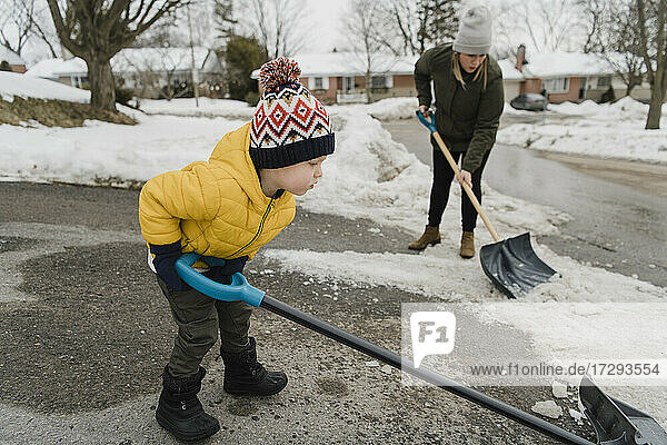 Son helping mother while shoveling snow on driveway