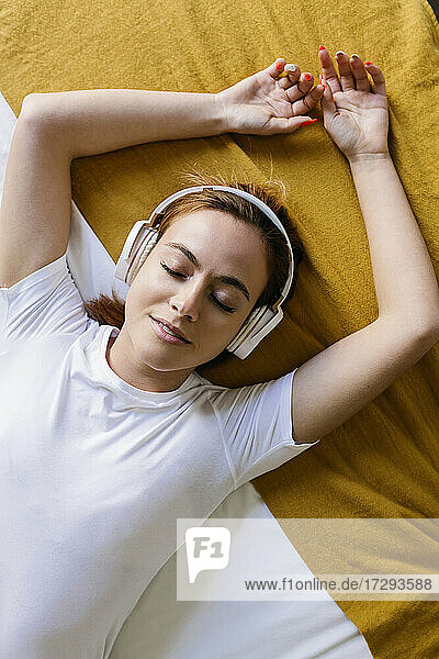 Junge Frau mit geschlossenen Augen hört Musik  während sie zu Hause auf dem Bett liegt