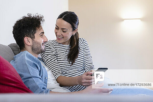 Smiling couple with smart phone sitting on sofa at home