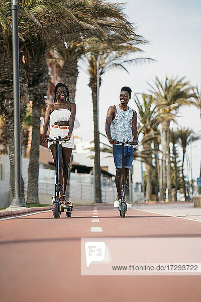Lächelndes Paar  das auf dem Fußweg einen elektrischen Roller fährt