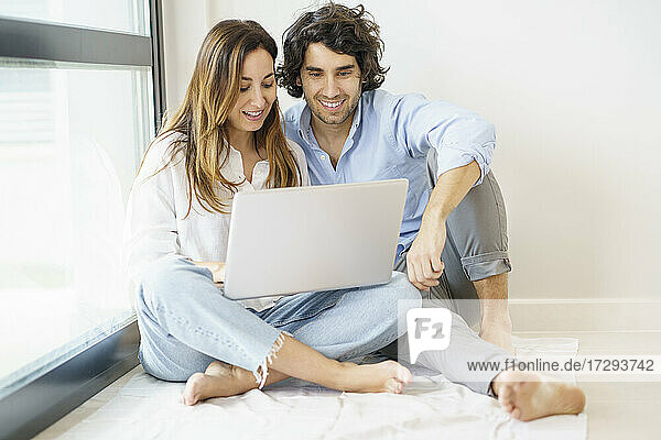 Smiling girlfriend and boyfriend using laptop together at home